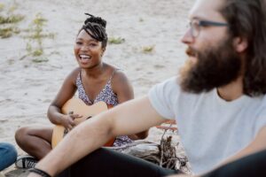 Deux adultes naturistes échangent calmement sur une plage, dans une ambiance conviviale et respectueuse.